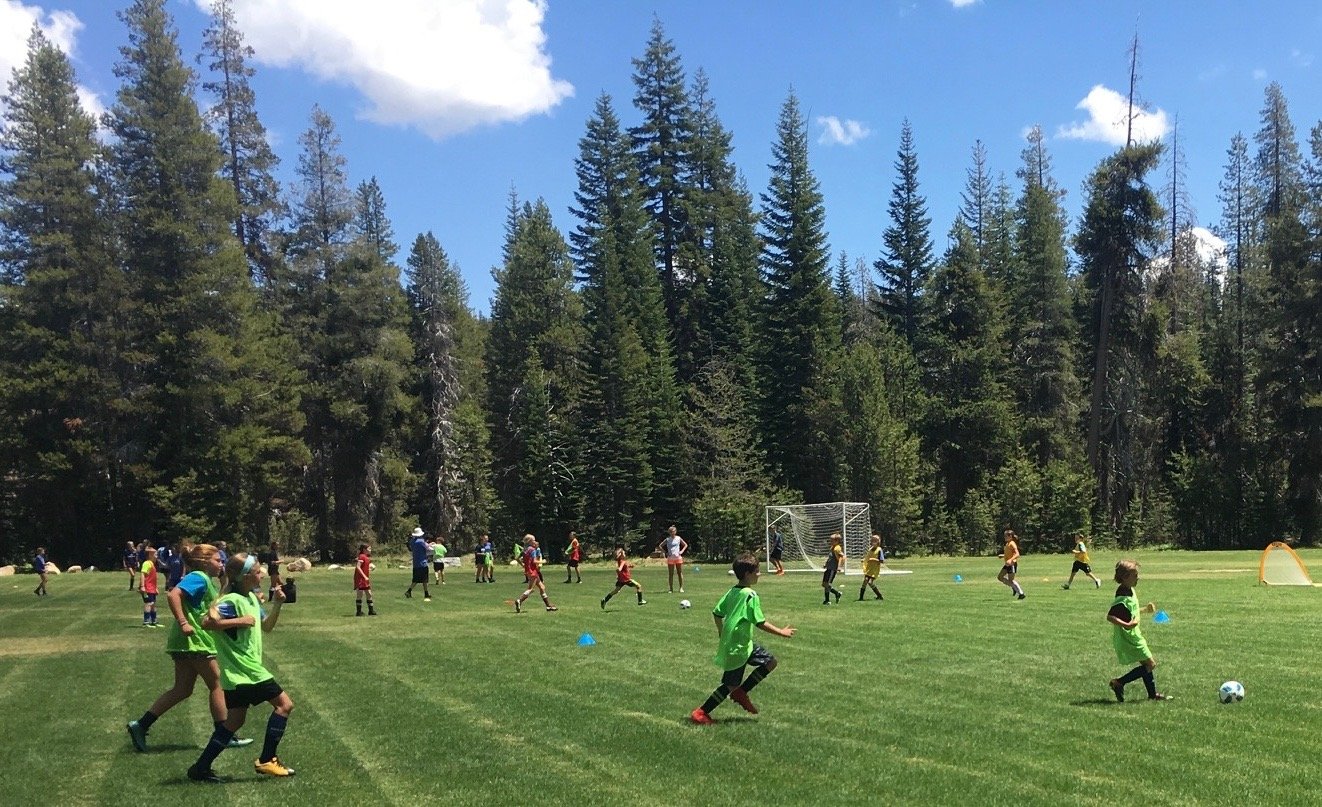 Campers playing soccer on a field surrounded by Sierra Nevada pines